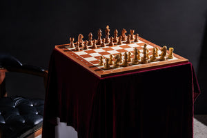 Ensemble échiquier en bois avec notation et pièces d'échecs Staunton naturelles et marron, disposé sur une table élégante avec une nappe rouge.