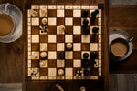 Charger l&#39;image dans la galerie, Partie de jeu d’échecs en bois sur échiquier pliant avec pièces sculptées – ambiance conviviale avec café
