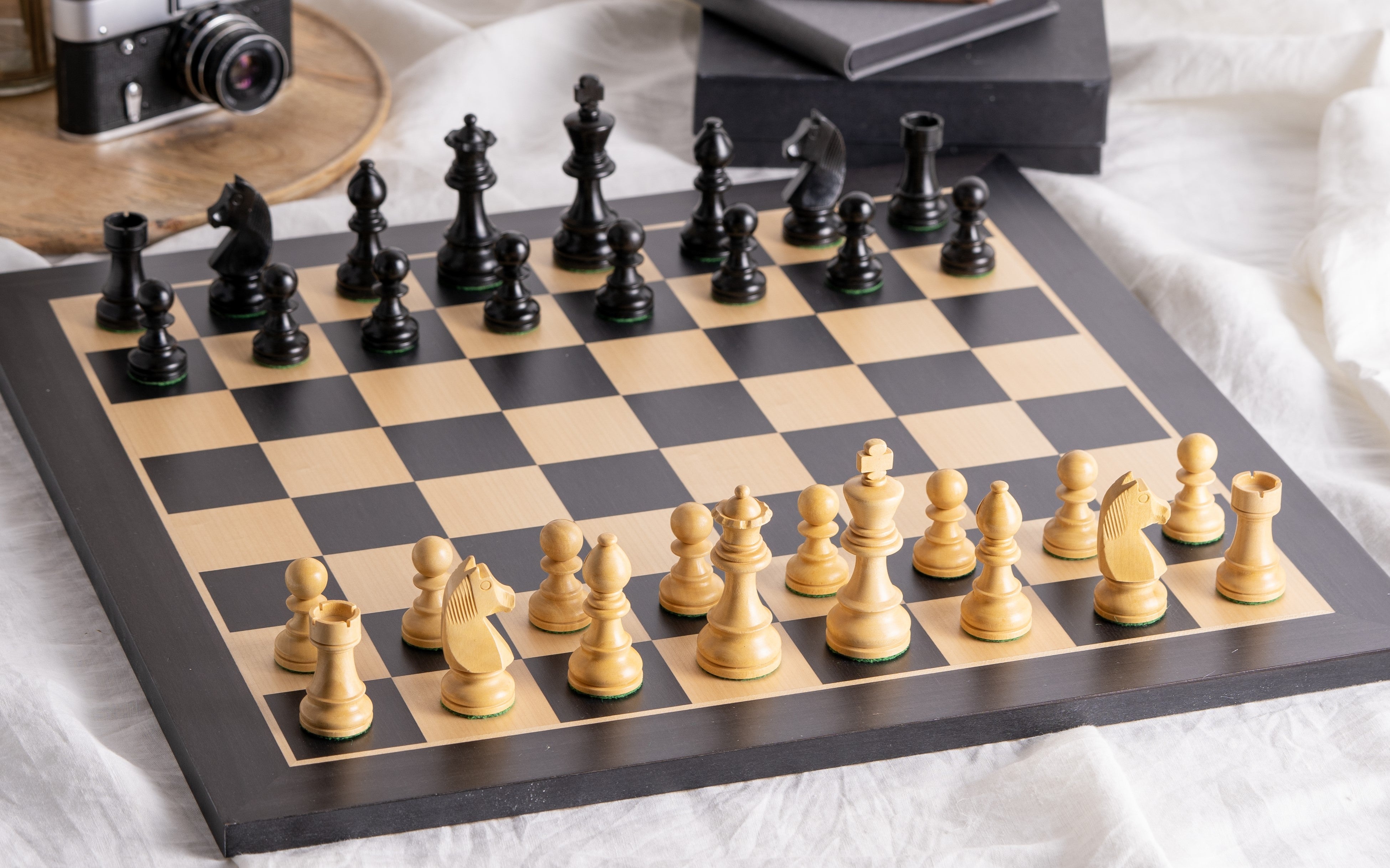 Zoom sur l’Échiquier & Pièces d'Échecs en Bois - Ensemble Staunton Noir et Blanc, avec pièces en bois sculpté noir et blanc sur un échiquier en bois clair et noir, ambiance élégante avec accessoires en arrière-plan.